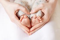 Die Füße eines Babys, die von den Händen der Mutter in Herzform umschlossen werden.